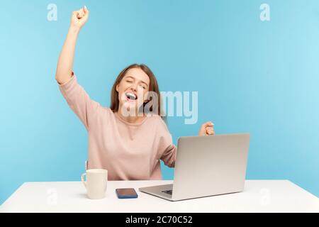 La giovane donna entusiasta si è rivolta alle mani e gridando per la gioia, celebrando il successo del business online, seduto in ufficio a casa. Foto Stock