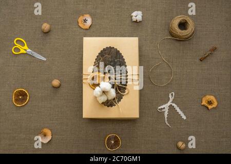 Natale Zero rifiuti stile di vita concetto. Disposizione piatta. Confezione regalo di carta artigianale, forbici, flagello di corda, fette di mela e arancia, cotone su sfondo di tela. Foto Stock