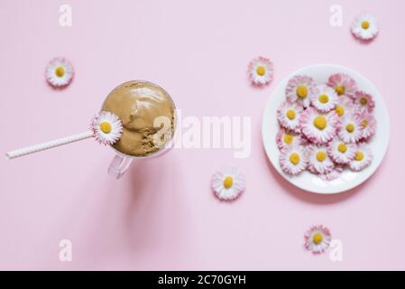 Caffè dalgona in una tazza trasparente con un tubo di carta, un piatto con fiori margherite. Vista dall'alto Foto Stock