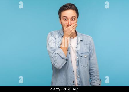 Non dico nessuno! Ritratto di uomo confuso spaventato in camicia di jeans lavoratore che copre la bocca con la mano, mantenendo terribile verità segreta, non vogliono parlare. Foto Stock