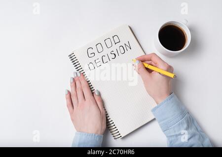 Vista dall'alto della donna scrive in taccuino l'iscrizione BUONA DECISIONE. Caffè del mattino e programmi di elenco. Foto Stock