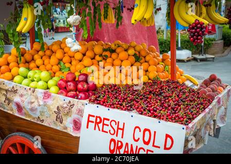 Un carrello nell'esposizione della frutta fresca per la vendita, compreso le banane, le arance, le mele, le ciliegie e più. Foto Stock