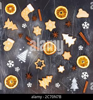 Biscotti allo zenzero natalizio, arancio secco, cannella, anice stellato e fiocchi di neve su fondo di pietra nera. Vista dall'alto. Foto Stock