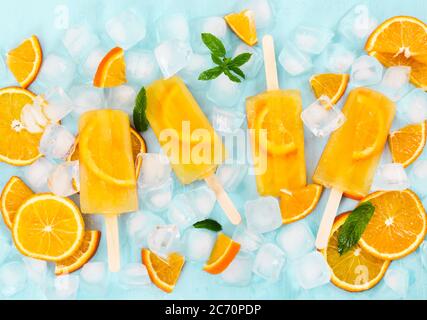 Frutta popsicle fatte in casa, cubetti di ghiaccio e fette di arancio su sfondo azzurro. Vista dall'alto. Foto Stock