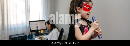 Ragazza che canta in travestimento mentre la madre telelavoro Foto Stock