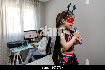 Ragazza che canta in travestimento mentre la madre telelavoro Foto Stock