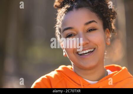 Ritratto esterno di bella felice gara mista biraciale Africano americana ragazza adolescente femmina giovane donna sorridente con denti perfetti indossando un arancione Foto Stock