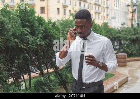 Uomo d'affari afro-americano in fretta. Uomo con caffè da asporto che parla al telefono in fretta Foto Stock