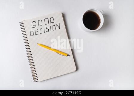 Scrittura a mano in notebook BUONA DECISIONE. Vista dall'alto della penna per blocco note e della tazza di caffè su sfondo bianco. Foto Stock
