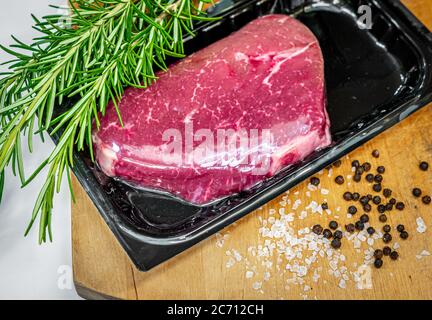 Bistecca di manzo in confezionamento sottovuoto e spezie su tagliere di legno Foto Stock