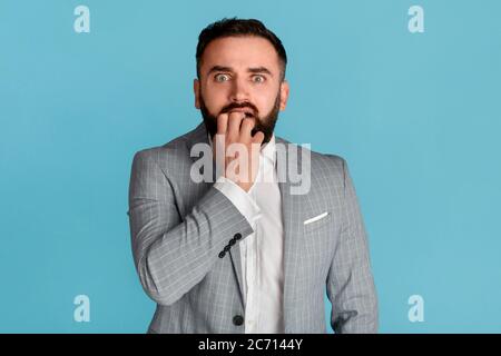 Gestione dello stress. Uomo d'affari spaventato che muta le unghie nel panico su sfondo blu Foto Stock