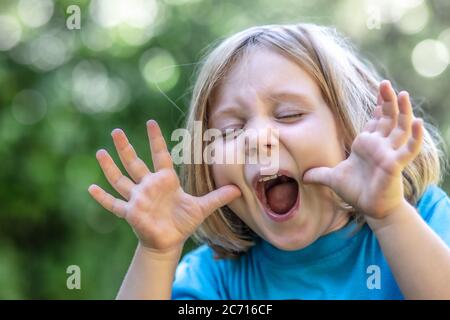 ritratto di una ragazza bionda che fa un volto divertente e divertente. Concetto di infanzia e felicità. Foto Stock