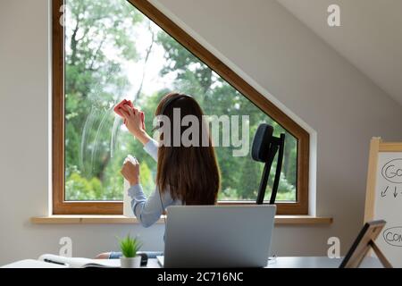 Donne lavano le finestre mentre su una chiamata di conferenza al lavoro. Nuovo concetto normale. Foto Stock