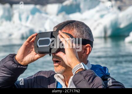 Uomo stupefatto che indossa occhiali VR con iceberg che galleggiano nella laguna di Jokulsarlon, Islanda. Foto Stock