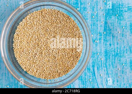 Grani di quinoa grezzi all'interno della ciotola trasparente, su tavola blu Foto Stock