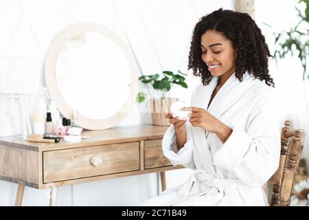 Skincare giornaliero. Bella donna nera usando crema idratante per la pelle a casa Foto Stock