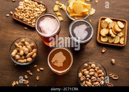 Birra scura, chiara, non filtrata in bicchieri e antipasti croccanti in piatti su tavola di legno Foto Stock