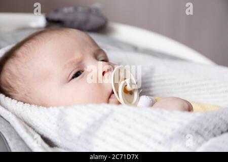 Un ritratto ravvicinato di una bambina appena nata, che giace in una culla e succhia un succhietto. Foto Stock