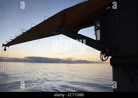 Silhouette di gru della nave mercantile container durante il tramonto passando oceano Atlantico in tempo con nuvole sullo sfondo . Foto Stock