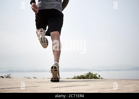 primo piano delle gambe di un corridore asiatico che corre sul mare, vista posteriore Foto Stock