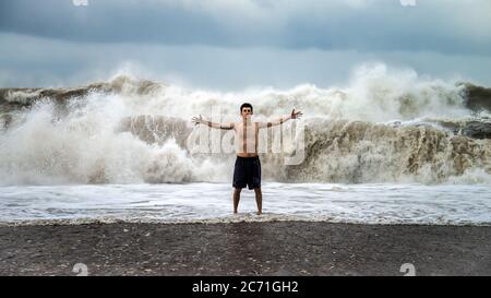 Antalya - Turchia - 17 ottobre 2013: Giovane uomo in piedi contro le onde del mare con spruzzi in un clima torbido Foto Stock