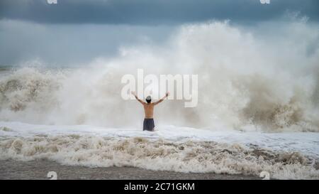 Antalya - Turchia - 17 ottobre 2013: Giovane uomo in piedi contro le onde del mare con spruzzi in un clima torbido Foto Stock