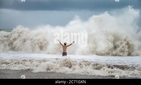 Antalya - Turchia - 17 ottobre 2013: Giovane uomo in piedi contro le onde del mare con spruzzi in un clima torbido Foto Stock