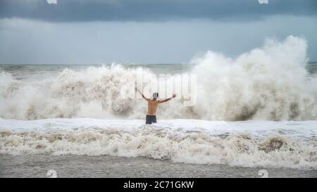 Antalya - Turchia - 17 ottobre 2013: Giovane uomo in piedi contro le onde del mare con spruzzi in un clima torbido Foto Stock