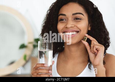 Assunzione giornaliera di vitamine. Happy Black Woman capsula di tenuta pillola e vetro dell'acqua Foto Stock