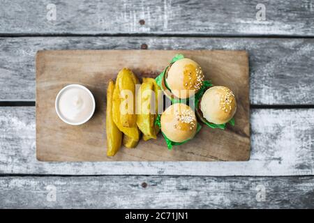 Tre mini hamburger con polpettine di manzo, patatine fritte e maionese su tavola di legno. Sfondo di tabella shabby invecchiato. Cibo insolito servire. Fast food e uno stile di vita malsano. Foto Stock