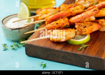 Spiedini o langostine di gamberi grigliati serviti con lime, aglio e salsa su fondo di cemento azzurro. Frutti di mare Foto Stock