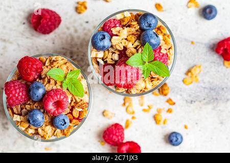 Parfait allo yogurt con muesli, lamponi e mirtilli in bicchieri, sfondo chiaro. Concetto di colazione salutare. Foto Stock