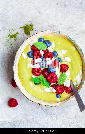 Coppa di frullato verde con frutti di bosco e cocco, fondo grigio. Concetto di cibo vegano sano. Foto Stock