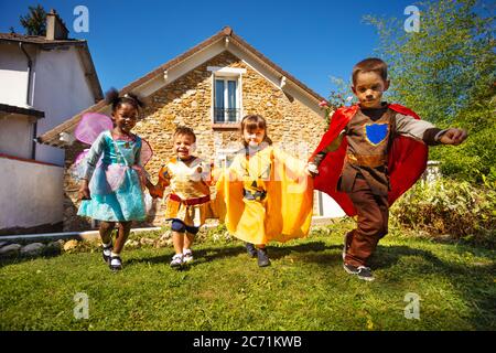 Gruppo di bambini piccoli corrono in costumi di Halloween sul prato prima che la casa tenga le mani Foto Stock