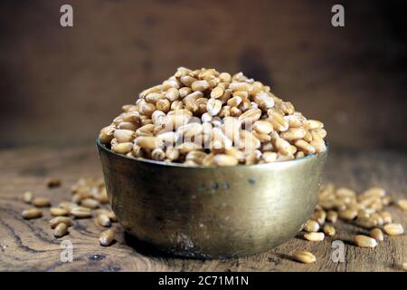 Pila di grano integrale organico. Grano fresco raccolto in una ciotola isolata su sfondo di legno. Grani di grano e farina di grano. Foto Stock