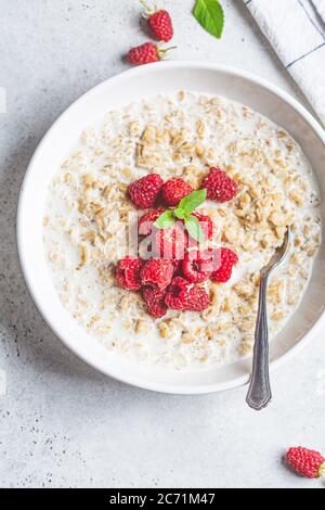 Prima colazione porridge di farinata d'avena con lamponi in un recipiente bianco. Concetto di colazione salutare. Foto Stock