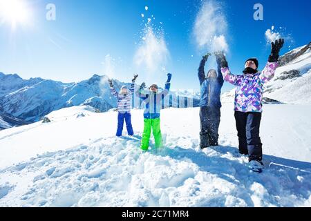 Quattro bambini felici di sciare gettano la neve in aria che si erono sopra la vista della catena montuosa superiore Foto Stock