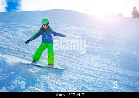 Foto d'azione rapida di un ragazzo che scende in discesa con vista da snowboard in equilibrio laterale con mani e polvere di neve illuminata dal sole Foto Stock