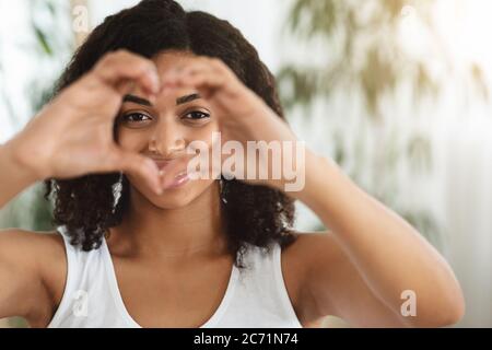 Mi amo. Donna felice che mostra cuore gesto e guardando attraverso di esso Foto Stock