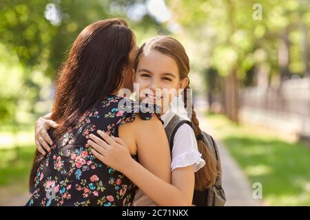 Adorabile studentessa con zaino abbracciando la sua mummia sulla strada per la scuola. Ritorno a scuola. Foto Stock