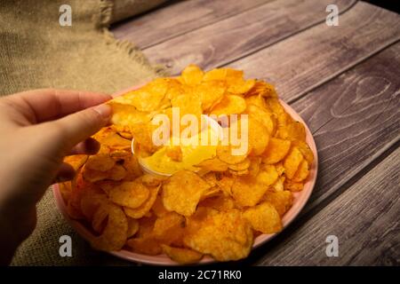 La ragazza prende un chip da un piatto rotondo con patatine e una pentola con salsa di formaggio al centro del piatto. Primo piano Foto Stock