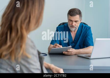 Il chirurgo senior consulta la giovane donna, il medico con paziente in ufficio medico. Foto Stock