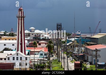 Guyana, Regione Demerara-Maharica, Georgetown, la Casa luminosa costruita in mattoni nel 1830 per sostituire una precedente costruzione in legno degli olandesi. Ha una forma ottagonale e si erge per 103 metri. È un monumento nazionale della Guyana. La torre dell'orologio del mercato di Stabroek è visibile a sinistra in lontananza. La vista si affaccia su Water Street verso i moli sul fiume Demerara. La centrale di generazione di energia elettrica è sulla destra in primo piano. Foto Stock