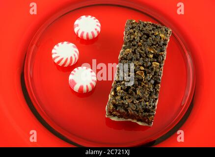 Barretta di nutrizione di cioccolato alla menta piperita con glassa e tre caramelle dure di menta piperita su piatto rosso Foto Stock