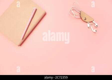 Diario beige con penna e cuffie su sfondo di carta rosa millenaria pastello. Concetto di istruzione, blogging. Vista dall'alto. Disposizione piatta. Stile minimalista. TEM Foto Stock