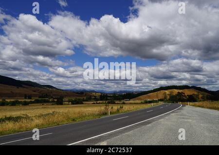 Tipica strada neozelandese sull'Isola del Sud con cielo blu e nuvole Foto Stock