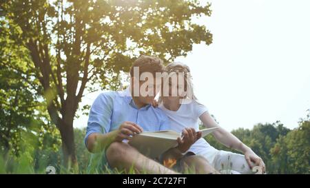 Un ragazzo e una ragazza stanno guardando un album di famiglia con foto nel parco sull'erba. Foto Stock