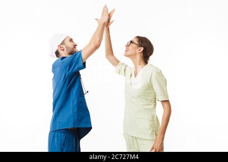 Giovane medico con fonendoscopio sul collo e sorridente infermiere in occhiali e uniforme con gioia dando cinque gesti l'uno all'altro su sfondo bianco Foto Stock