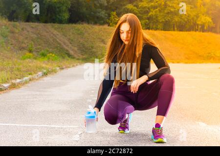 Bella ragazza giovane in corso di formazione con acqua. L'atleta donna prende una pausa per bere acqua. Allenamento estivo. Fitness, persone e stile di vita sano Foto Stock