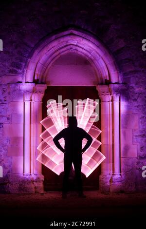 Sessione di pittura leggera in un luogo mistico. Forma circolare con una sciabola leggera. Silhouette di un uomo con una curva leggera dietro di lui. Architettura gotica. Foto Stock